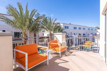 Two orange chairs are on a patio with a palm tree.